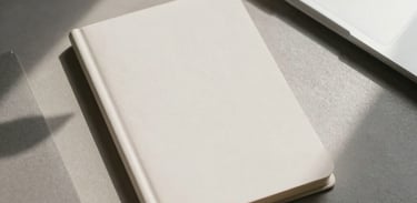 Overhead shot of a minimalist workspace with neutral-colored stationery and a single leaf shadow, soft and focused lighting.