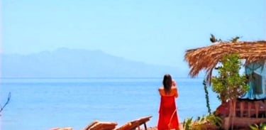 Woman in red sarong taking a photo of the Red Sea and beach bungalows at Bedouin Star Sinai, Egypt
