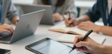 A close-up photograph of a hands-on digital learning workshop. Professional North American / International setting. Students collaborating over tablets and books. Bright, airy, and professional atmosphere.