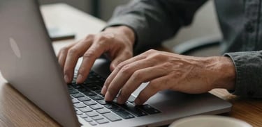 A close-up of a person's hands typing on a laptop in a well-lit North American office, with a cup of coffee nearby, representing productivity and a reliable work environment, charcoal gray tones.