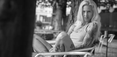 Outdoorshooting einer blonden Frau mit Tattoos sitzt entspannt auf Bank in schwarz-weiss Portrait von Fotograf in Chur