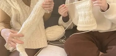 Two women holding up their cream beginner knitting projects at The Paddock and Purl Studio.