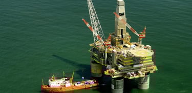 Vista aérea de uma plataforma petrolífera marítima e um navio de abastecimento ao lado.