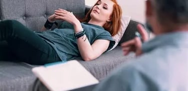 femme allongée sur un canapé en état d'hypnose et son thérapeute de dos qui la guide