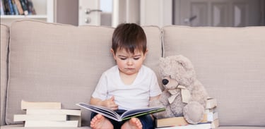 un petit garçon assis sur un canapé qui lit un livre avec un ours en peluche