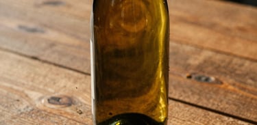 Warm editorial close-up of a wine bottle on a rustic wooden table at golden hour, soft natural light, rich earthy tones, 35mm film look