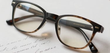 A pair of reading glasses resting on a letter with elegant cursive handwriting. Sophisticated, intimate, and professional photography with a soft focus.
