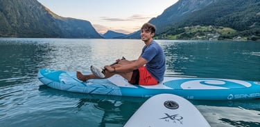 Man paddleboarding on a stand-up board in a calm Norwegian fjord surrounded by mountains