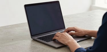 Hands typing on a sleek laptop on a clean concrete desk, soft natural overcast daylight, professional minimalist setup