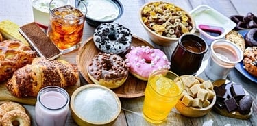 Variety of sugary foods including donuts, pastries, soda, cereal, and sweets on a table.