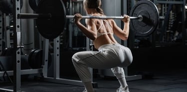 A fit woman performs a barbell back squat in a gym power rack for leg strength training.