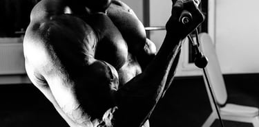 Black and white photo of a muscular bodybuilder performing cable bicep curls in a gym.