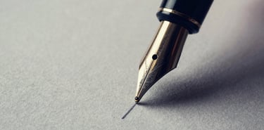 Extreme close-up of a high-quality fountain pen nib drawing a fine line on heavy textured paper, dark navy shadows, subtle warm gold highlights, editorial architectural photography style, 35mm
