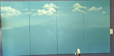 Four stretched canvas panels painted in a seashore blue now with fluffy swirling white clouds painted into the blue.
