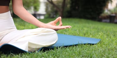 A woman practicing yoga and meditation on a blue mat in a lush green park.