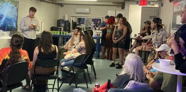 A group of people sitting and standing in a basement community room attending an educational presentation.