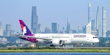 Hawaiian Airlines jet parked on a tarmac beside blue water and the city skyline in the background