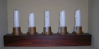 Block of padauk wood holding five brass fire nozzles used as candlestick holders.