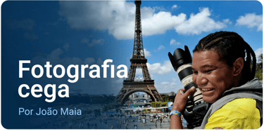 João segura uma câmera fotográfica profissional com uma lente acoplada. Ao fundo, a torre Eiffel.