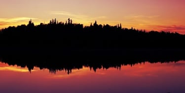 photo: reflection of fiery sunset and trees on a placid lake in Alaska