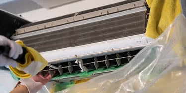 uma pessoa limpando um ar condicionado com uma luva amarela