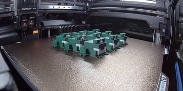 Bambu Lab 3D printer bed with a batch of green blocky toy frogs printed on a textured PEI plate.