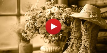 Rustic sepia still life featuring vintage cowboy boots, a wide-brimmed hat, and fresh spring flowers.