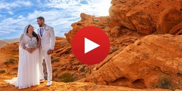 A bride and groom pose during a desert wedding at Valley of Fire State Park with a bighorn sheep on red rocks.