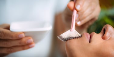Esthetician applying a professional chemical peel facial treatment to a client using a fan brush.