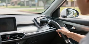 A man uses a portable vacuum cleaner brush attachment to clean dust from a car dashboard.