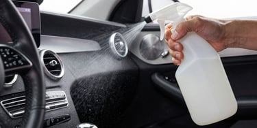 Hand spraying cleaning solution onto a modern luxury car interior for professional auto detailing.