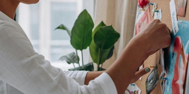 A creative woman pinning photos and inspiration to a cork mood board in a home office.