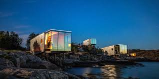Modern glass cabins perched on rocky cliffs overlooking the ocean at dusk for a luxury retreat.