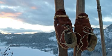 two skis stuck upright in the snow with leather shoes