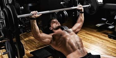 Muscular man performing an incline barbell bench press for chest strength training in a gym.