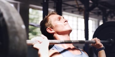 Focused athlete performing a barbell overhead shoulder press at a fitness gym.