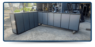 A sleek, modern gray aluminum cabinet is displayed outdoors, with construction materials visible in the background