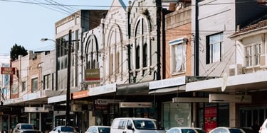 Historic commercial storefronts and parked cars on a sunny Willoughby road in Sydney.