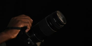A person's hand holding a professional Canon DSLR camera with a long telephoto lens against a black background.
