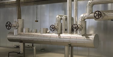Insulated industrial steel pipes and valves in a modern mechanical room for HVAC or steam systems.
