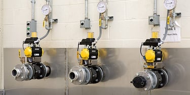 Three industrial ball valves with pneumatic actuators and pressure gauges mounted on a wall.