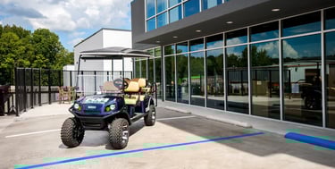 Custom blue lifted golf cart parked in a modern dealership lot with large glass windows.