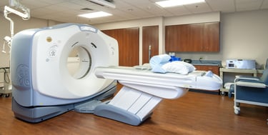 A modern GE medical CT scanner in a sterile hospital diagnostic imaging room with an adjustable patient table.