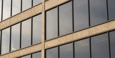 Detail of modern architectural glass facade reflecting overcast sky, clean lines, minimalist editorial photography, warm sand tones