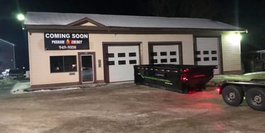 Pushaw Energy building at night with a large black dumpster parked in front of three white garage doors.
