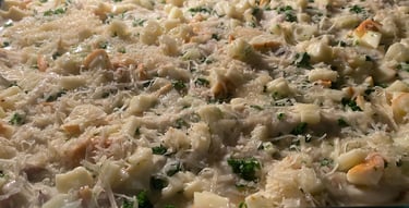 Close-up of uncooked creamy chicken casserole in a glass baking dish, topped with shredded cheese, diced chicken, and herbs