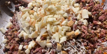 Close-up of a pan filled with ground meat and mushroom mixture, topped with shredded parmesan cheese and diced apples, ready