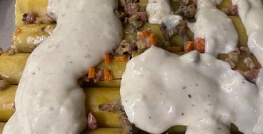 Uncooked cannelloni pasta tubes filled with meat and vegetable stuffing, topped with white bechamel sauce before baking.