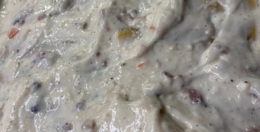 Close-up of creamy white lasagna sauce with vegetables and herbs being spread in a baking dish.