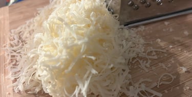 Freshly grated parmesan cheese piled on a wooden cutting board next to a stainless steel box grater.